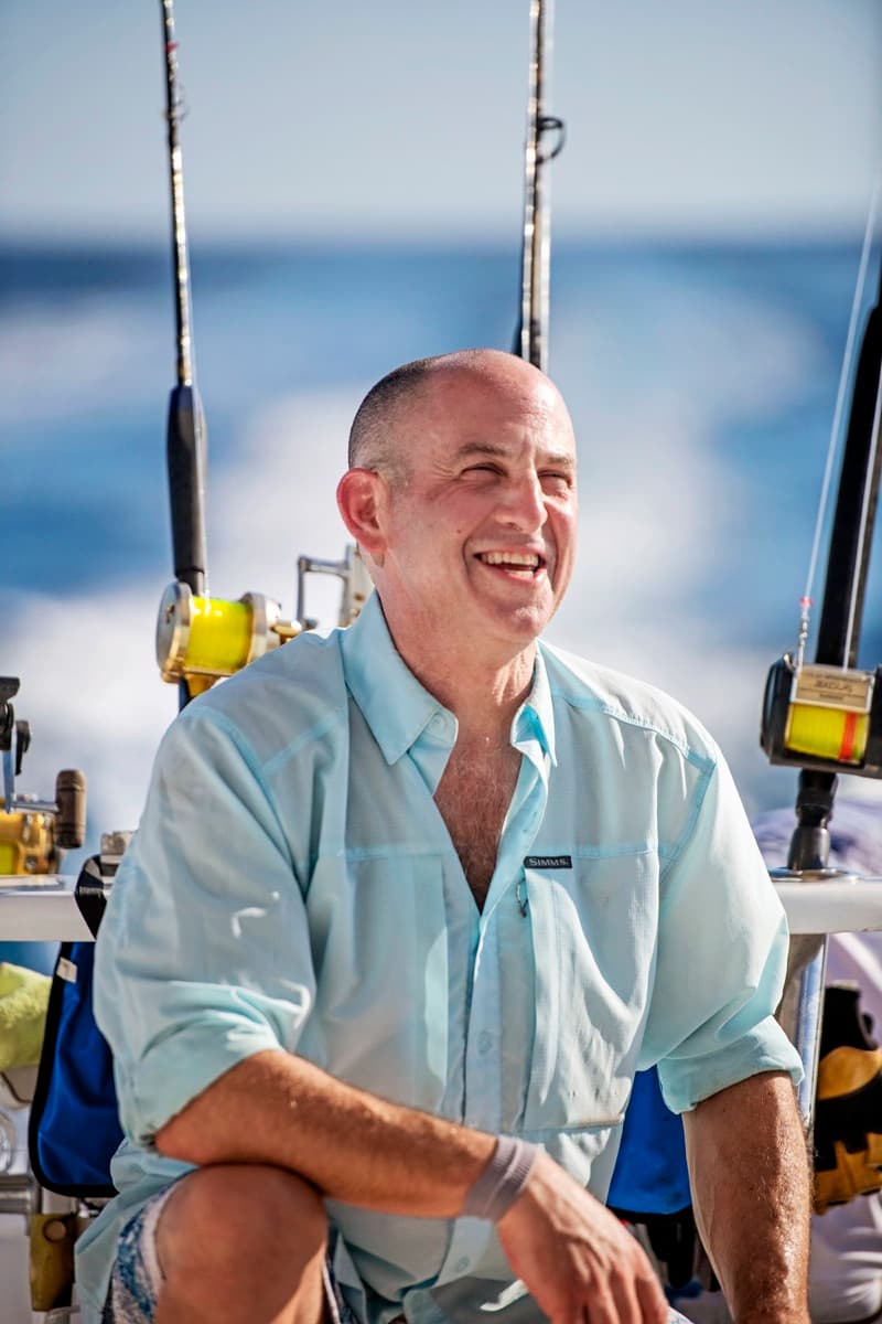 Warren Werbitt smiling aboard a fishing boat surrounded by fishing rods at sea